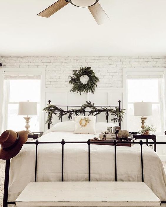 a cozy farmhouse bedroom with white brick walls, fir branches and a forged bed looks serene and chic