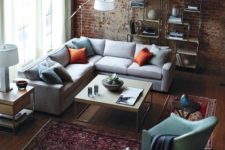 a cozy industrial living room with a red brick wall, a wooden floor, boho rugs, neutral furniture and metal shelving units
