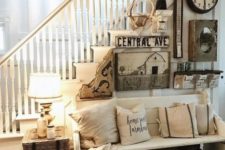 a cozy vintage farmhouse entryway with a wooden bench, pillows, a gallery wall with lots of different items and a woven box plus a lamp