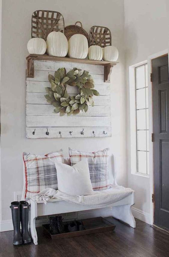 a cute farmhouse space with a wooden sign with a wreath, a selection of pumpkins and baskets, a white bench with pillows