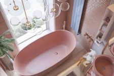a cute pink bathroom with a pink bathtub, sink, tiled walls and touches of gold here and there