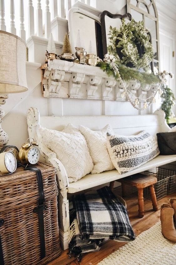a farmhouse ebtryway with a shabby chic bench, a basket with clocks, pillows and blankets, a shelf with greenery and vintage mirrors