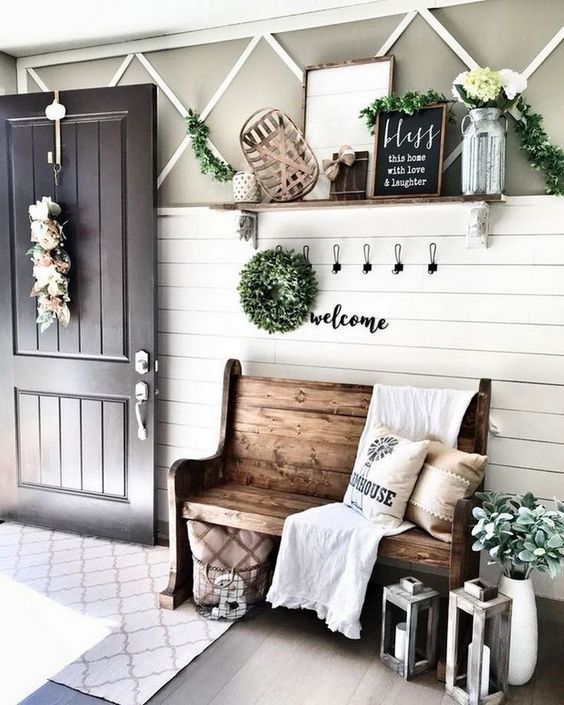 a farmhouse entryway with a wooden bench, candle lanterns, signs, blooms and greenery and a large mirror
