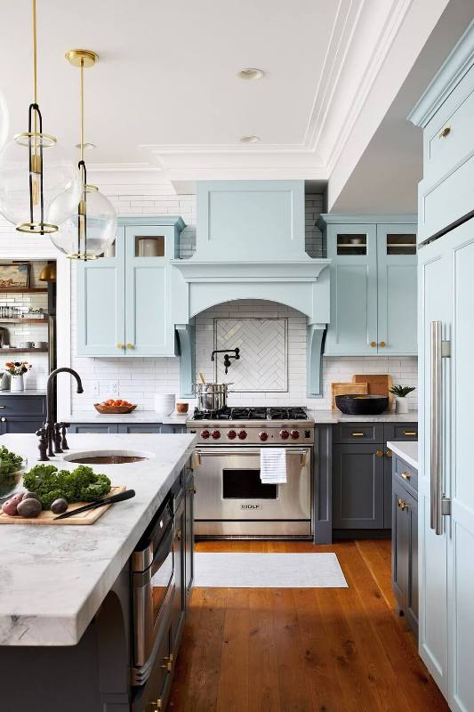 a farmhouse kitchen with graphite grey and light blue cabients, a white herringbone tile backsplash and pendant lamps