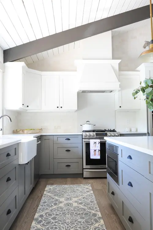 a farmhouse kitchen with white and pale blue shaker style cabinets, a white tile backsplash and a printed rug