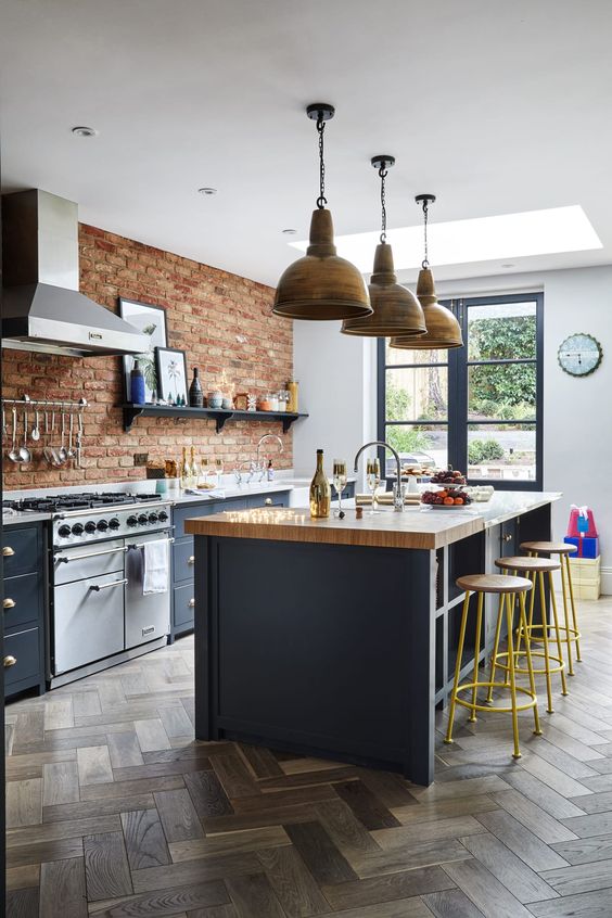 a farmhouse meets industrial kitchen with red brick walls, grey cabinets with stone countertops, vintage lamps and stools