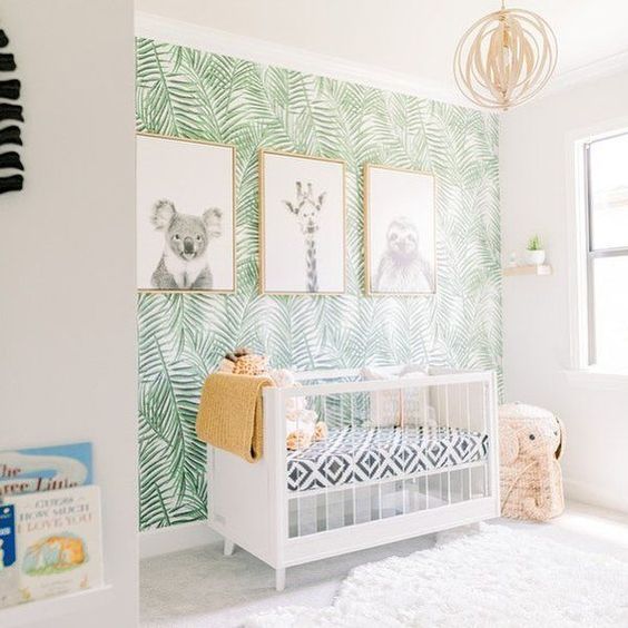 a funny tropical nursery with a tropical leaf print wall, black and white artworks, an elephant basket and a sphere chandelier