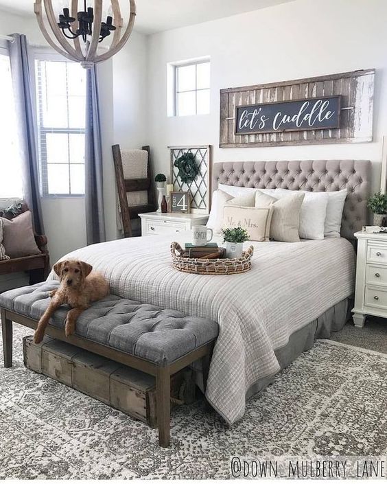a gorgeous farmhouse bedroom with an upholstered bed and bench, with touches of reclaimed wood and greenery