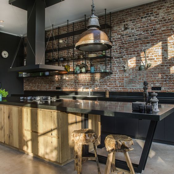a gorgeous industrial kitchen with red brick walls, black cabinets, a large wooden kitchen island and a vintage lamp