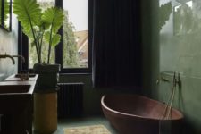 a gorgeous tropical bathroom with green walls and a floor, a copper tub, potted plants and a glass enclosed shower