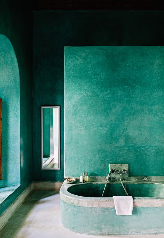 a green Moroccan style bathroom with everything of concrete and plaster, with a small mirror and built in tub