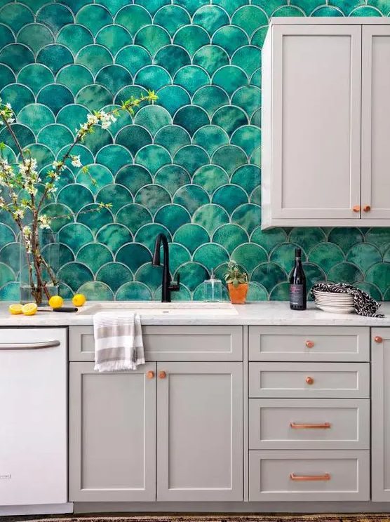 a grey kitchen with shaker cabinets, white stone countertops, a bold green fishscale tile backsplash and copper handles