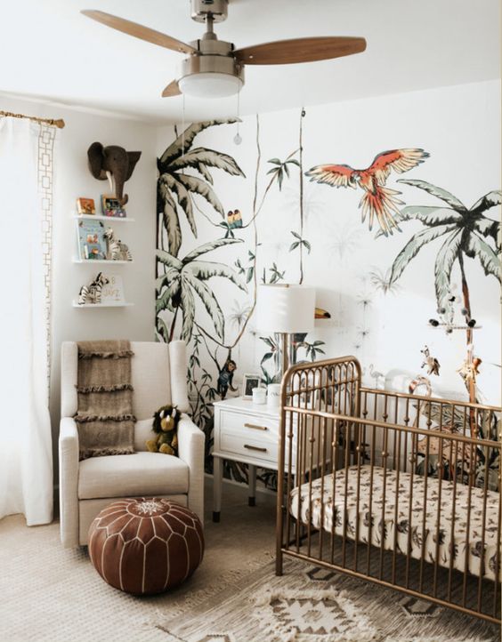 a jungle themed nursery with a fun printed wall, tropical bedding, a leather ottoman, cute jungle themed toys