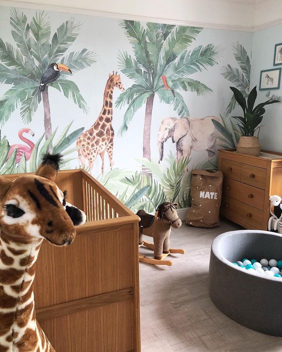 a jungle themed nursery with a statement animal wall, animal toys, potted plants and cute furniture