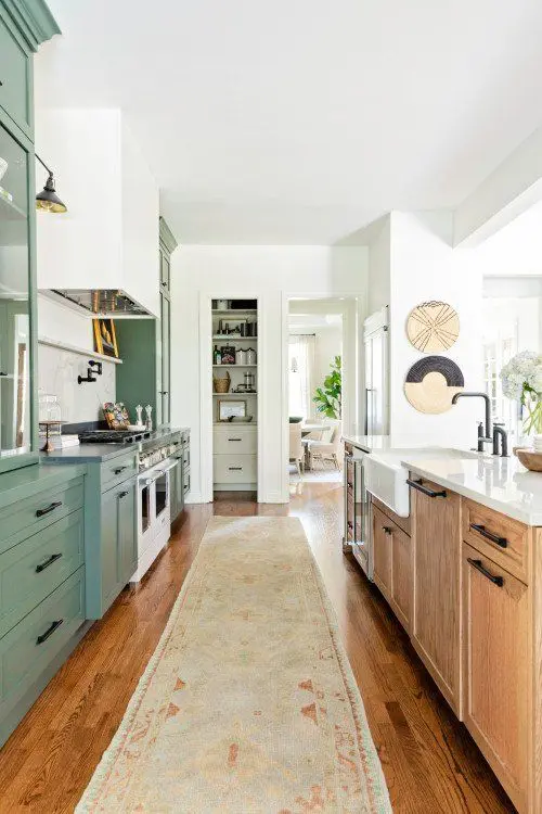 a kitchen with green and stained cabinets, a white tile backsplash, black handles and some lovely decor
