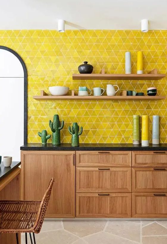 A light stained kitchen with black countertops, open shelves and a super bold yellow triangle backsplash and bold accessories