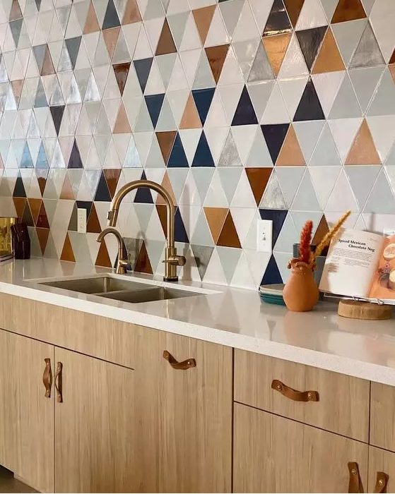 a light-stained kitchen with neutral stone countertops, a bold geo tile wall and leather handles and brass fixtures