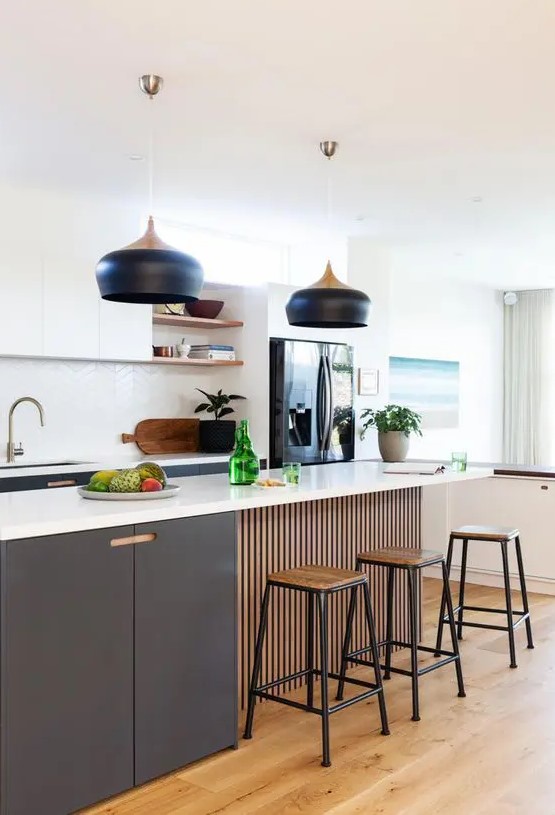a lovely contemporary kitchen with graphite grey and white cabinets, a white chevron tile backsplash, catch black pendant lamps