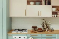 a lovely two-tone kitchen with nude and mint blue cabinets, stained handles, a woven pendant lamp, a white subway tile backsplash