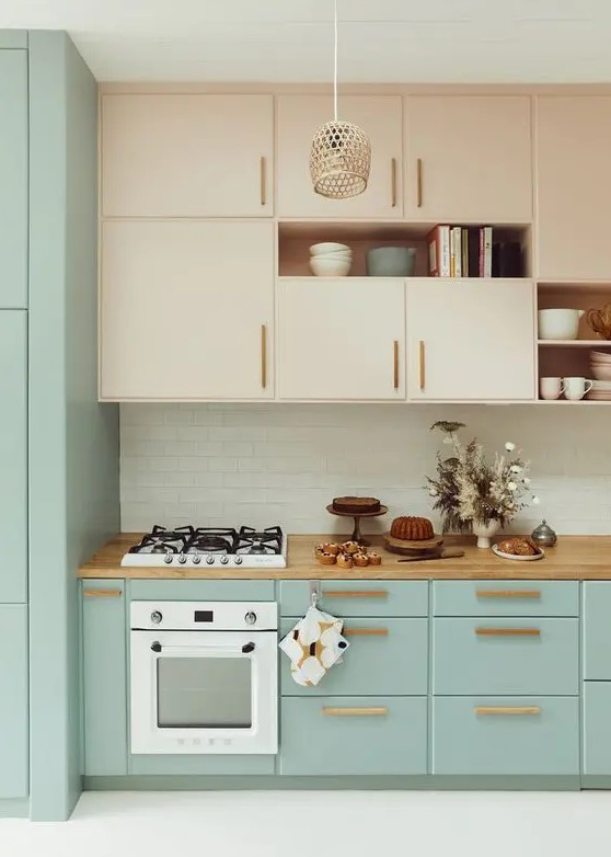 A lovely two tone kitchen with nude and mint blue cabinets, stained handles, a woven pendant lamp, a white subway tile backsplash