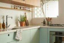 a mid-century modern two-tone kitchen with stained and mint green cabinets, white countertops, a penny tile backsplash