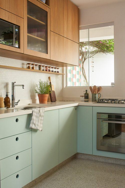 a mid-century modern two-tone kitchen with stained and mint green cabinets, white countertops, a penny tile backsplash