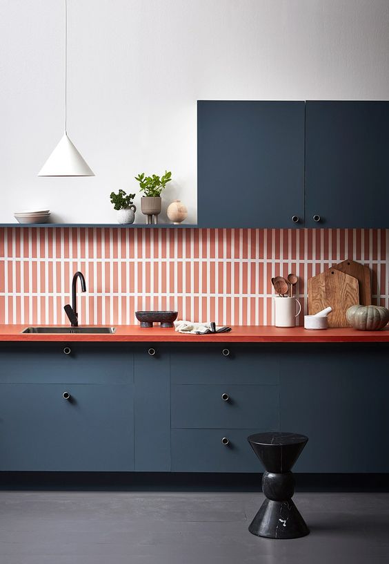 a minimalist graphite grey kitchen with red countertops, an orange stacked tile backsplash and black fixtures