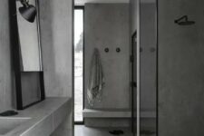 a minimalist grey bathroom done in concrete, with black fixtures and touches, with a large mirror and a window
