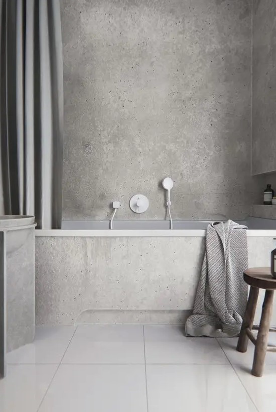 a minimalist grey bathroom done with concrete and tiles, with a niche for storage, a large curtain, a concrete vanity and a wooden stool