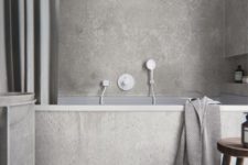 a minimalist grey bathroom done with concrete and tiles, with a niche for storage, a large curtain, a concrete vanity and a wooden stool
