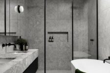 a minimalist grey bathroom done with grey marble tiles, glass doors, touches of black for drama and a skylight