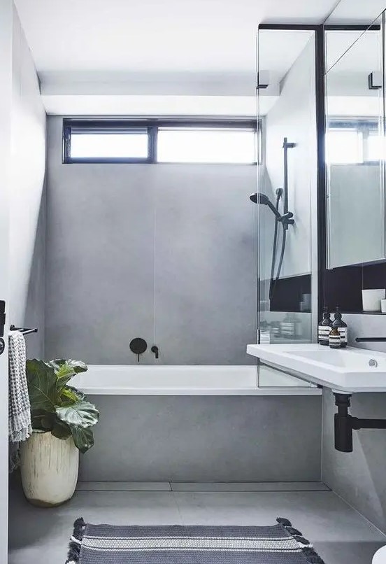 a minimalist grey bathroom done with large scale tiles, with black fixtures and potted plants plus a wall mounted sink