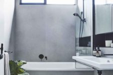 a minimalist grey bathroom done with large scale tiles, with black fixtures and potted plants plus a wall-mounted sink