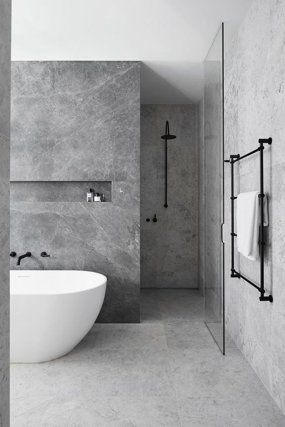 a minimalist grey marble bathroom with darker and lighter tiles, a free standign tub and black fixtures for a more contemporary look
