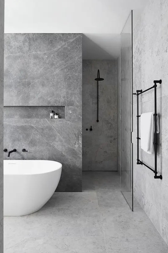 a minimalist grey marble bathroom with darker and lighter tiles, a free-standing tub and black fixtures for a more contemporary look