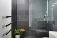 a minimalist grye bathroom clad with tiles, with a glass enclosed shower, white appliances and potted greenery