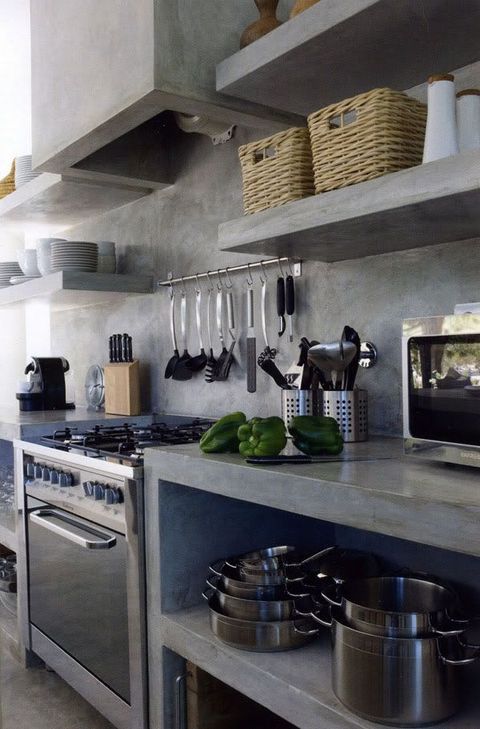 a minimalist industrial kitchen with concrete walls, cabinets, shelves and hood, metal appliances and some tableware