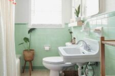 a mint green bathroom with a wlal-mounted sink, a toilet and a bathtub, a bold rug and a pompom curtain