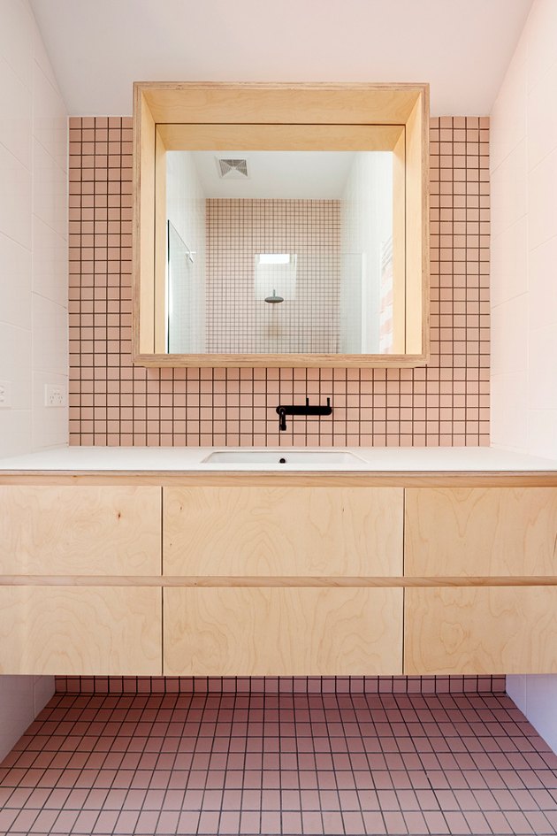 a modern bathroom clad with pink tiles and black grout, with light-colored MDF furniture and black fixtures