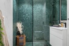 a modern boho bathroom clad with white marble and green penny tiles in the shower, a floating vanity and a basket