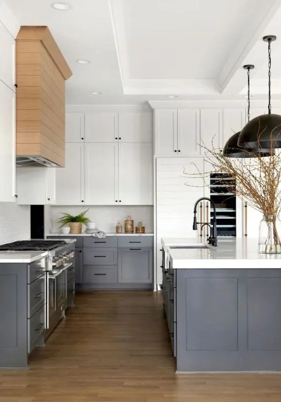 a modern farmhouse kitchen with white upper cabinets, dark grey lower ones, white countertops and a backsplash, black pendant lamps