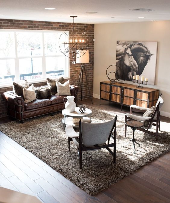 a modern industrial living room with a faux brick wall, modern furniture, a wood and metal dresser and a chic sphere chandelier