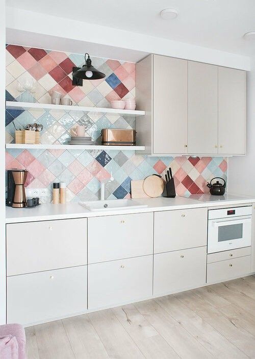 a modern neutral kitchen with white countertops and a colorful diagonal tile backsplash, which adds color