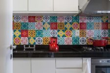 a modern white kitchen with black countertops and a super colorful eclectic tile backsplash is amazing