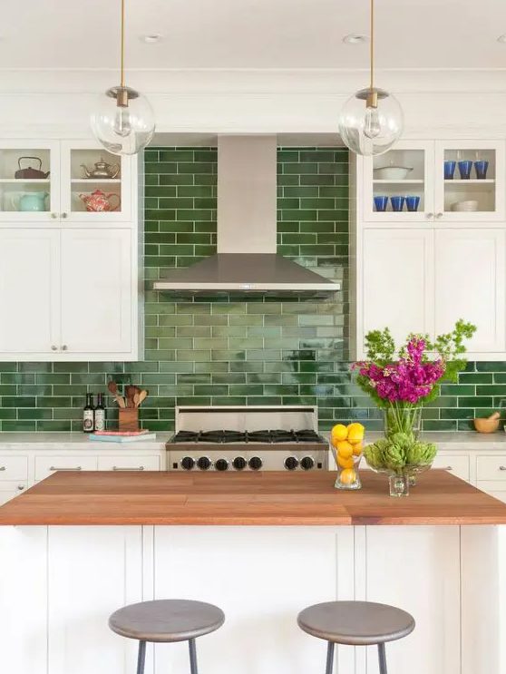 a modern white kitchen with shaker cabinets, a green tile backsplash, a kitchen island with a butcherblock countertop and pendant lamps