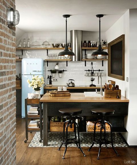 a monochromatic kitchen with light wooden countertops, black lamps and stools and crates for storage