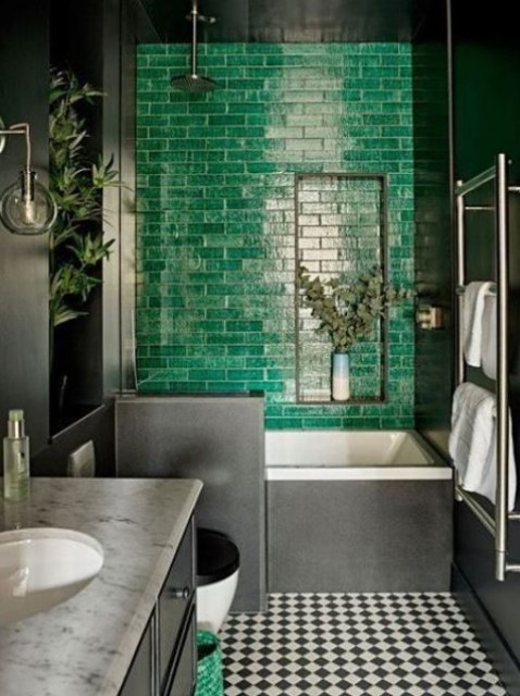 a moody bathroom with a statement emerald tile wall, a checked floor and a marble countertop looks super bold