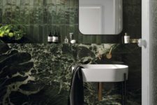 a moody green bathroom clad with tiles and marble, with tile floors, catchy appliances and a mirror on the wall