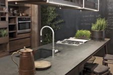 a moody industrial kitchen with wooden cabinets, a chalkboard wall, a wooden kitchen island and pendant lighting with storage