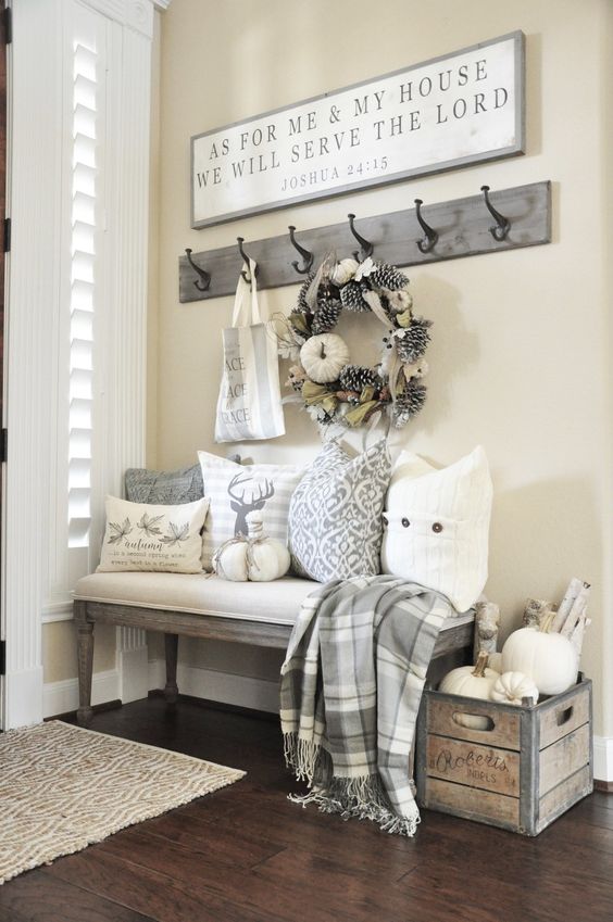 a neutral farmhouse entry with a large sign, a box with pumpkins, printed pillows, a pinecone and pumpkin wreath and a plaid blanket